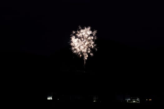 A firework rocket in the sky on a mountain at night, a few illuminated houses in the foreground,A firework rocket in the sky on a mountain at night, a few illuminated houses in the foreground