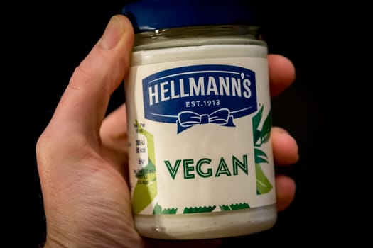 Antwerp, Belgium, October 2019: Illustrative Editorial: Hand holding Hellmann's Vegan and plant-based mayonnaise spread on black background.