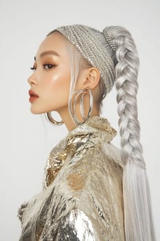 A model showcases a stylish braided hairstyle, wearing a shimmering gold jacket and large hoop earrings, highlighting her unique look.