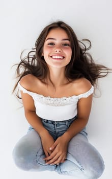 A cheerful woman with long hair sits on a light background, smiling while wearing casual attire. Her joyful expression radiates happiness.