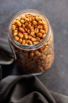 Roasted salted corn snack in jar on a black table.