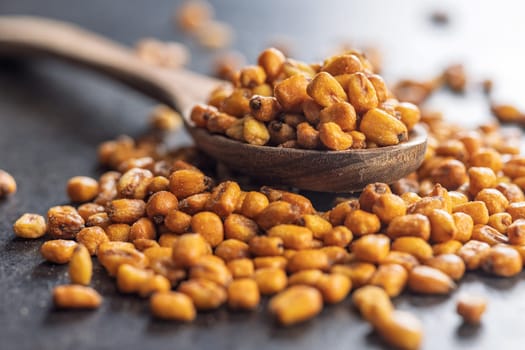 Roasted salted corn snack on spoon on a black table.