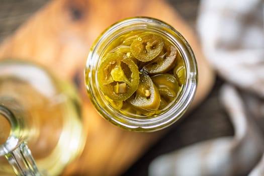 Pickled sliced jalapeno peppers in jar on a wooden table. Top view.