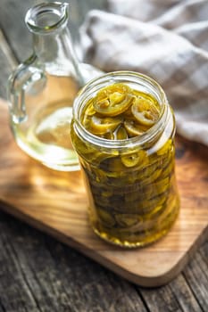 Pickled sliced jalapeno peppers in jar on a wooden table.