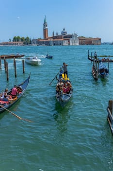 Venice, Italy - July 26, 2024: Gondolas against the San Giorgio island in Venice, Italy. Gondola is the most attractive tourist transport in Venice. Traveling and vacation in sunny Venice.