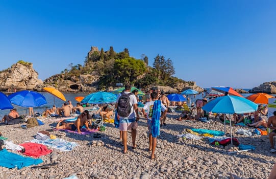 Taormina, Italy - August 11, 2024: People on the beach of Taormina with Isola Bella island on the background. Sicilia, Italy