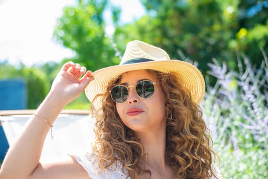 smiling young woman with straw hat and sunglasses enjoying the sun in the garden