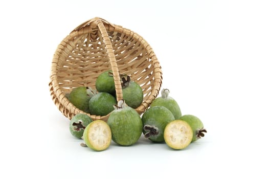 A collection of fresh feijoa fruits spilling from a wicker basket. The vibrant green color and texture of the fruits are highlighted against a white backdrop