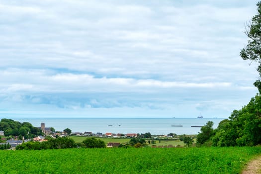 A beautiful view of a small town with the sea in the background. The sky is cloudy, but the overall mood is peaceful and serene, Normandy, France