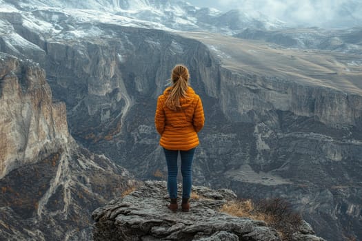 Woman standing on a cliff edge is enjoying a breathtaking view of a vast canyon and mountain range