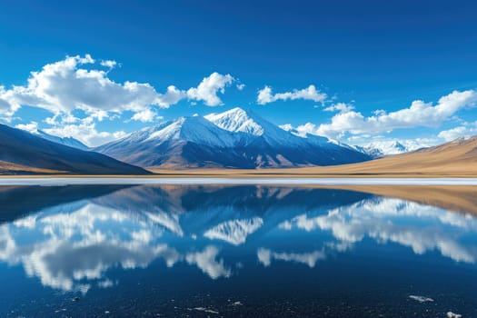 Snow capped mountain reflecting perfectly in serene lake on a sunny day with blue sky and clouds