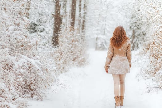 Young woman is enjoying a snowy day in the woods, taking a walk on a path covered in fresh snow