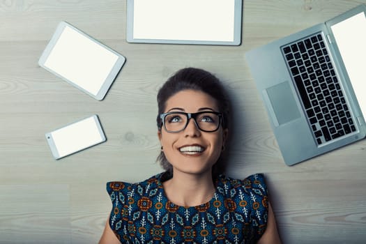 Smiling woman lying on wooden floor with digital devices, offering blank screens for customization