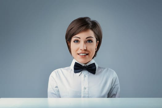 Confident young waitress in stylish bow tie smiles behind restaurant counter, exuding professionalism and elegance