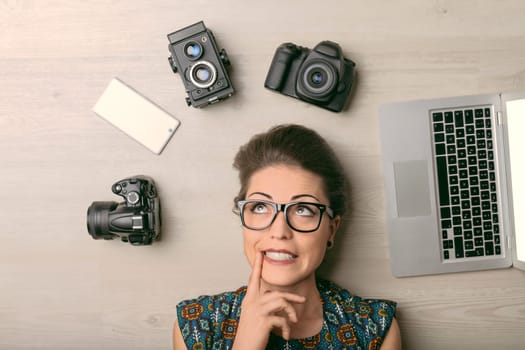 Young photographer lies on the floor, deep in thought, surrounded by camera and laptop, planning her next shoot with determination and creativity