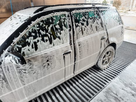 A car is covered in a thick foam layer during a wash in a public self-service car wash station
