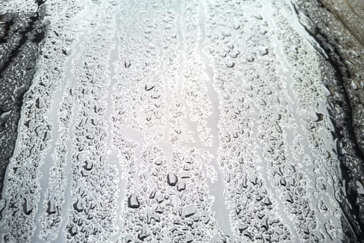 rain water drops on a bonnet of a black car during rainy day, full-frame closeup view