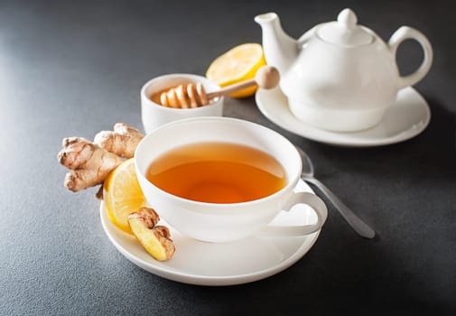 Cup of hot ginger tea with fresh ginger root and lemon on grey background close up