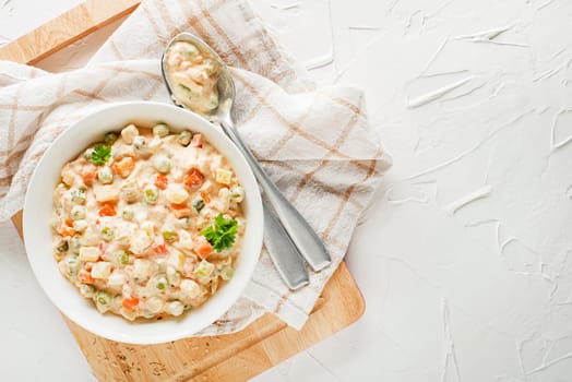 Bowl of russian salad or olivier or french salad with vegetables and egg dressed with mayonnaise on white table close up