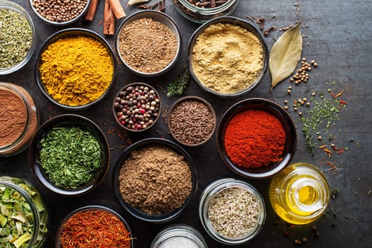 Colorful herbs and spices for cooking dishes. Indian and Asian spices. On grey stone background. Top view.