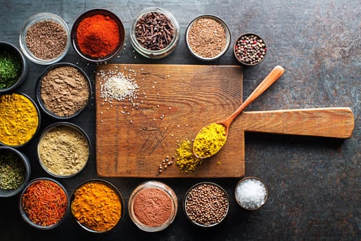 Colorful herbs and spices for cooking meal. Indian and Asian spices on cutting board background for free space for menu or recipes. Top view.