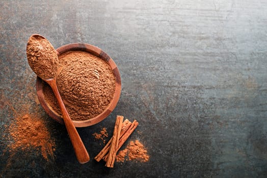 Aromatic cinnamon powder and sticks with spoon on grey background close up