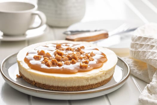Cheesecake with caramel topping on plate on a white table.