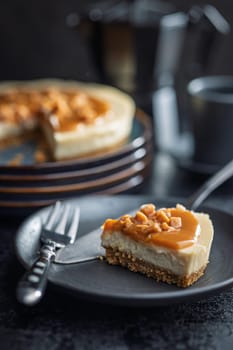 A cut piece of cheesecake with caramel topping on plate on black