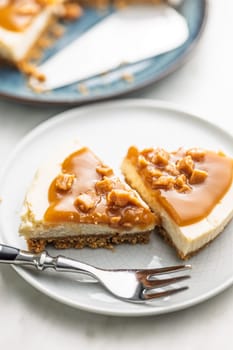 A cut piece of  cheesecake with caramel topping on plate on a kitchen table.
