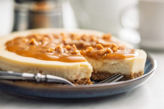 A cut piece of  cheesecake with caramel topping on plate on a kitchen table.