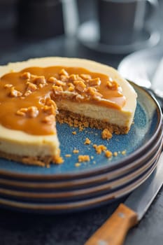 A cut piece of cheesecake with caramel topping on plate on a black table.