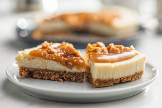 A cut piece of  cheesecake with caramel topping on plate on a kitchen table.