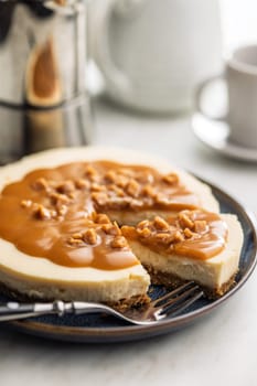 A cut piece of  cheesecake with caramel topping on plate on a kitchen table.
