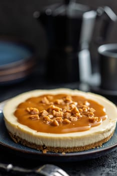 Cheesecake with caramel topping on plate on black table.