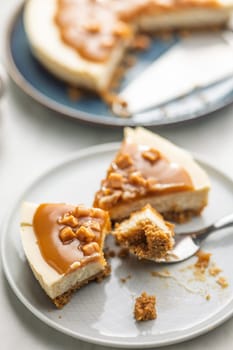 A cut piece of  cheesecake with caramel topping on plate on a kitchen table.