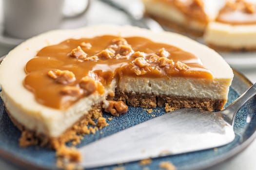 A cut piece of  cheesecake with caramel topping on plate on a kitchen table.