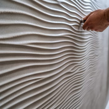 A hand uses a tool on a textured wall with wavy patterns. The design creates a 3D effect.