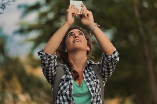 Young woman with a backpack takes pictures on her smartphone while hiking in a lush forest, fully immersed in the joy of her outdoor adventure