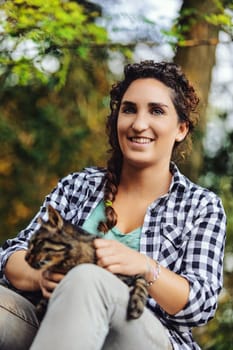 Young woman in a forest, holding her tabby cat, smiling peacefully, radiating love and companionship, embodying happiness and serenity