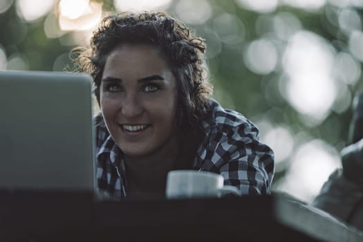 Young woman instructor is smiling while teaching online using her laptop outdoors, passing on knowledge to her students in a virtual classroom setting