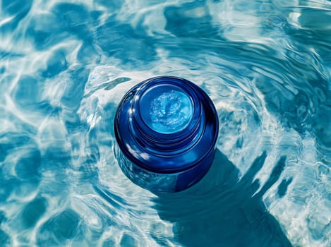 A rounded blue container rests atop calm water, reflecting the sunlight. The ripples create a shimmering effect around it.