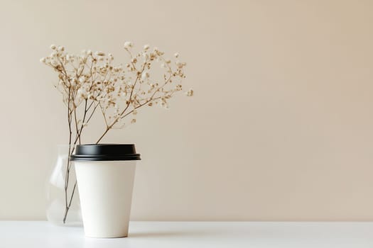 A simple setup features a white coffee cup next to a small vase of dried flowers on a light background, creating a cozy ambiance.