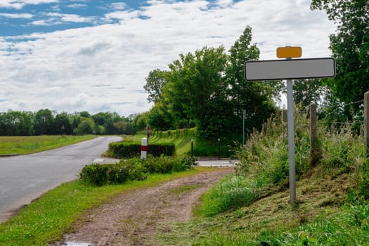 A road with an empty sign. The road is surrounded by trees and grass, Normandy, France