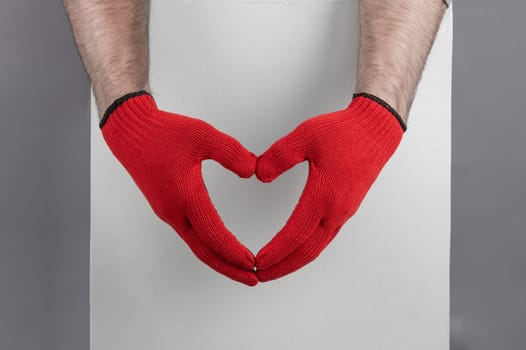 Close-up of hands wearing red gloves creating a heart shape against a gray sweater, symbolizing love, and care.