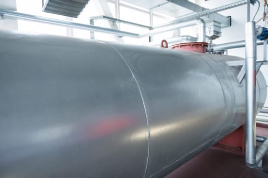 Outdoor Atmospheric Pressure deaerator. Close-up of a large metallic tank in an industrial facility, featuring pipes and equipment.