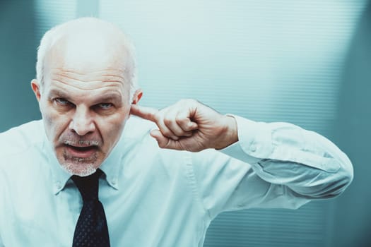 Stressed senior business manager plugging ears with fingers while shouting in disagreement, expressing frustration and anger over a conflict at work in a corporate office setting