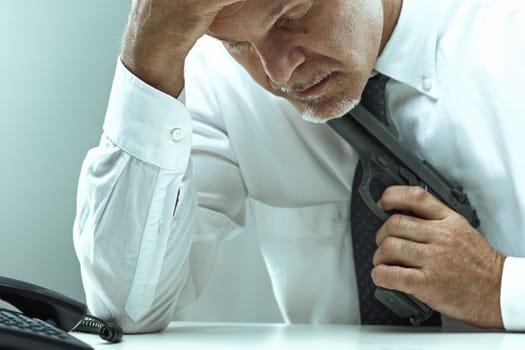 Stressed mature businessman sitting at his desk, gripping a gun under his chin, grappling with thoughts of suicide following a devastating financial crisis and overwhelming despair