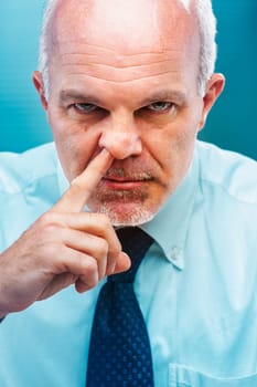 Close-up portrait of a mature businessman humorously picking his nose with his finger, showcasing a funny and irreverent gesture that highlights bad manners in a corporate setting