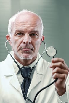 Portrait of a mature doctor in a white coat, confidently holding a stethoscope while looking seriously at the camera in a well-equipped medical setting, conveying expertise and professionalism