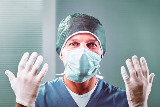 Mid adult surgeon wearing a surgical mask and gloves, confidently displaying hands in a clean hospital operating room, highlighting expertise and commitment to patient care